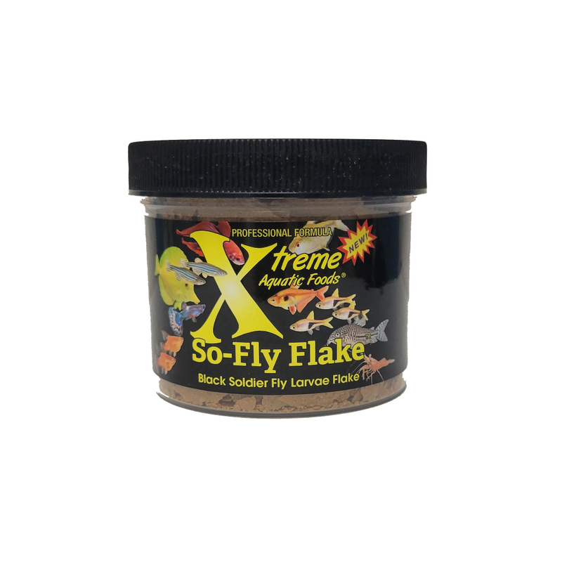 A clear plastic jar containing Xtreme 14g So-Fly Flake fish food, with a black lid and a label featuring the product name and branding with various different tropical fish.